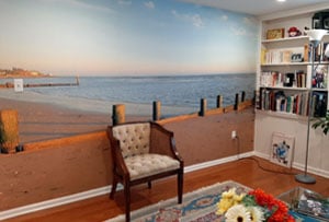 A beach wallpaper mural gives an expansive view to this home office and den, with a pier in the foreground and the horizon beyond the ocean in the background; it makes this small room seem enormous.