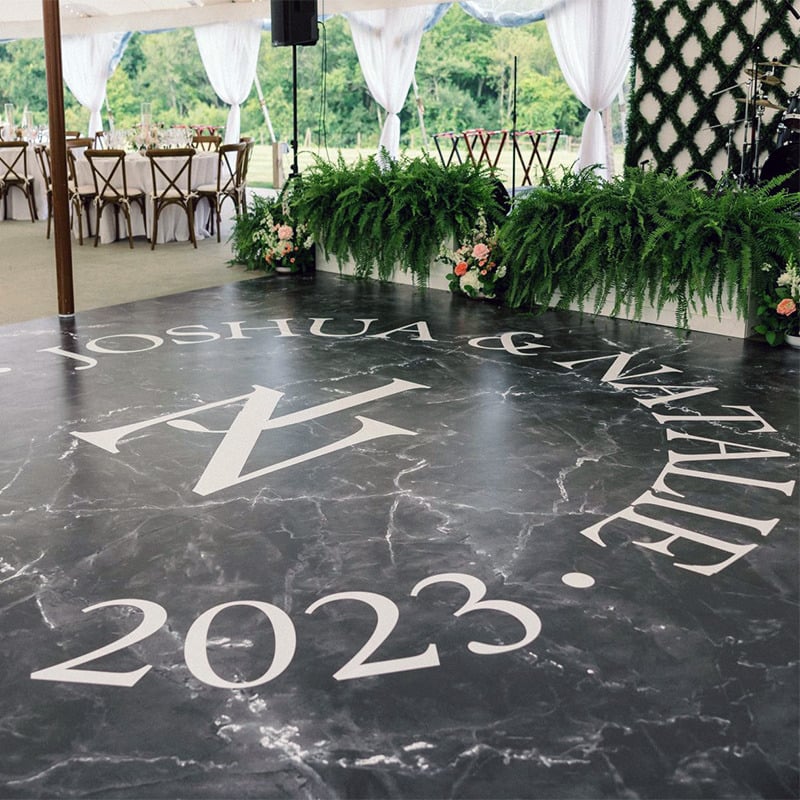 A bride and groom's names and wedding date have been printed in white typography on a vinyl dance floor wrap that has the sophisticated look of black marble.