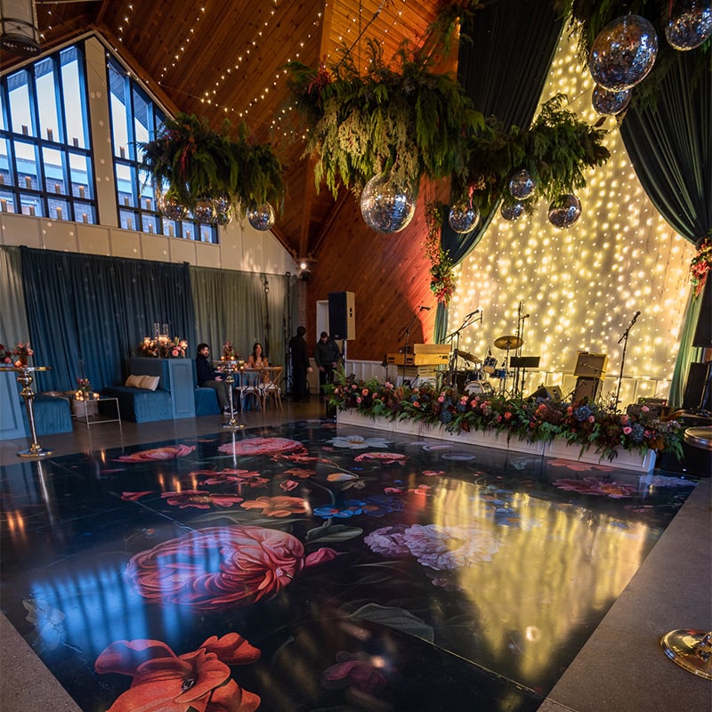 Oversized painted flowers on a dark background were printed on this wedding's dance floor wrap to match the floral arrangements and linen and drapery colors of this intimate yet sophisticated banquet venue.