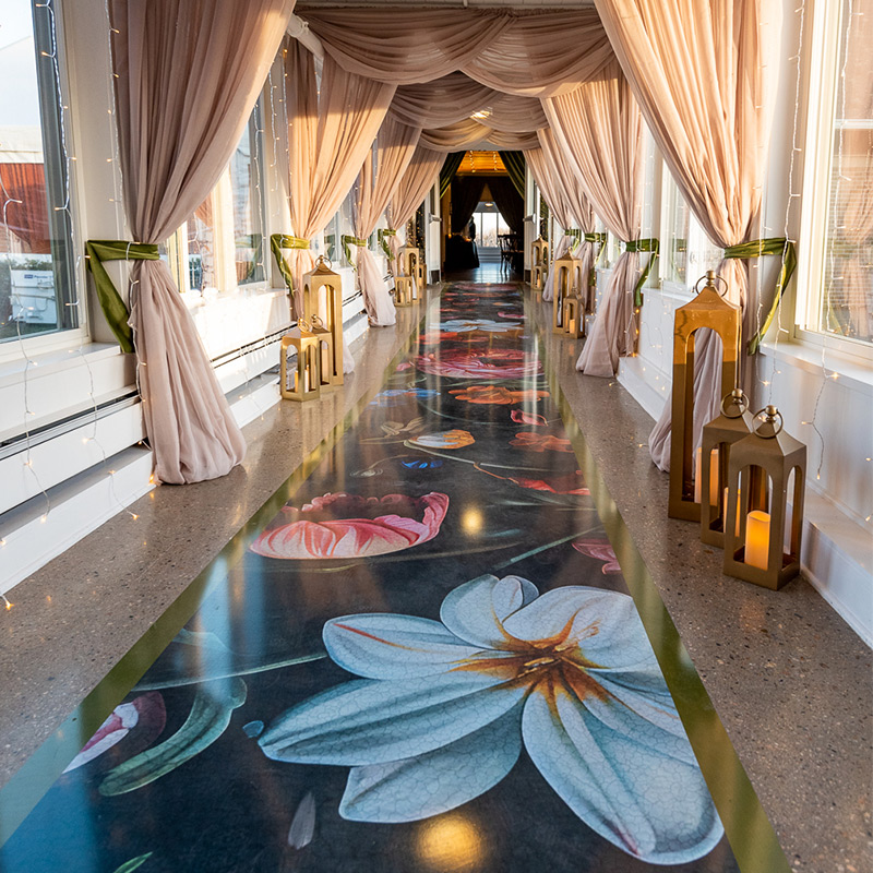A beautiful and artistic floral pattern has been printed on this vinyl floor wrap that serves as a runner through the long corridor connecting the lobby and reception room at this wedding venue.