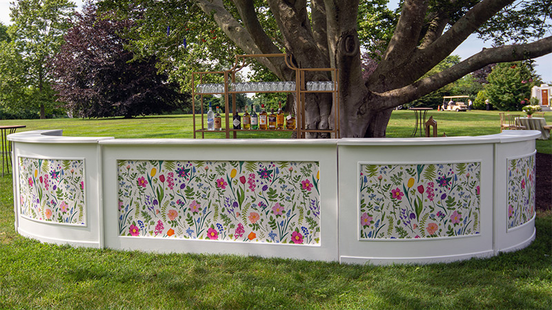 Colorful spring flowers were custom printed on easy to apply & easy to remove wallpaper that was inserted into the panels of this portable service bar at an outdoor wedding venue.
