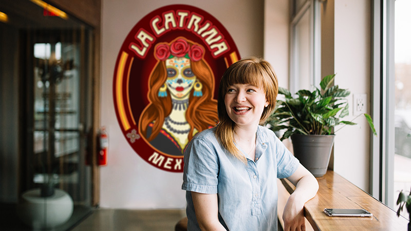 This photo shows us a diner at a window seat at a casual Mexican restaurant. Behind her is a contour-cut wall decal displaying the mascot and name of the cafe. This wallpaper mural draws in foot traffic and serves as a background for social media selfies.