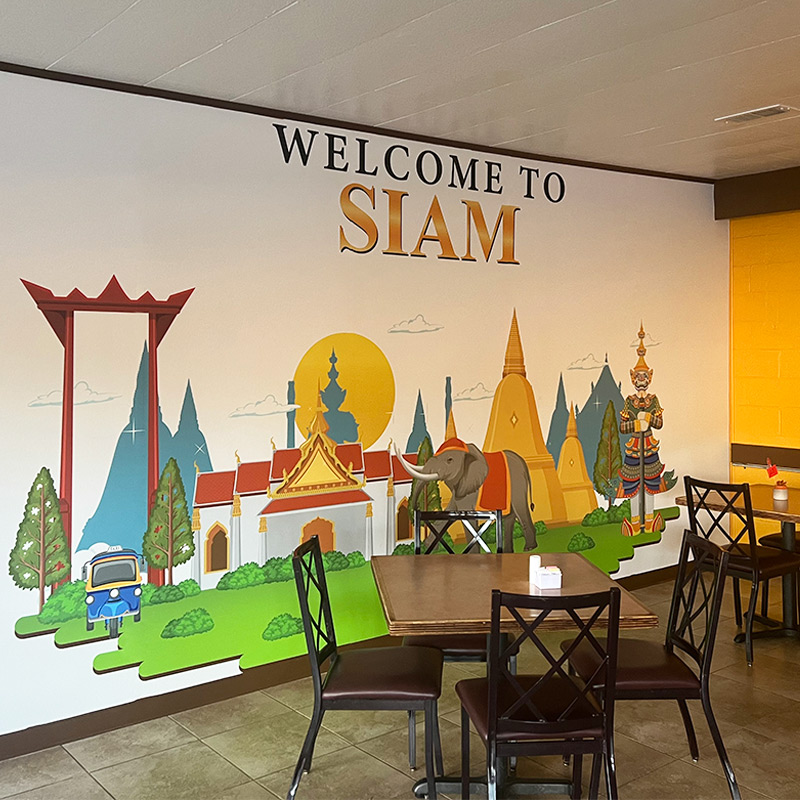 Siam Thai Cuisine, a quick serve eatery in western North Carolina, has a main dining area that is dominated by a full sized wallpaper mural featuring the restaurant's name (in their own font) and illustrated images of Thai and Siamese cultural icons.