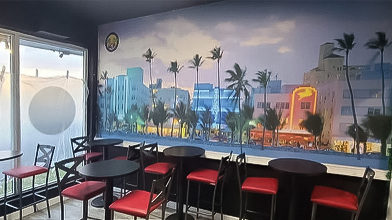 A colorful wallpaper mural of Ocean Drive on Miami Beach is a focal point of the dining room at Eat My Way Miami, a fusion restaurant specializing in Caribbean and Soul Food.