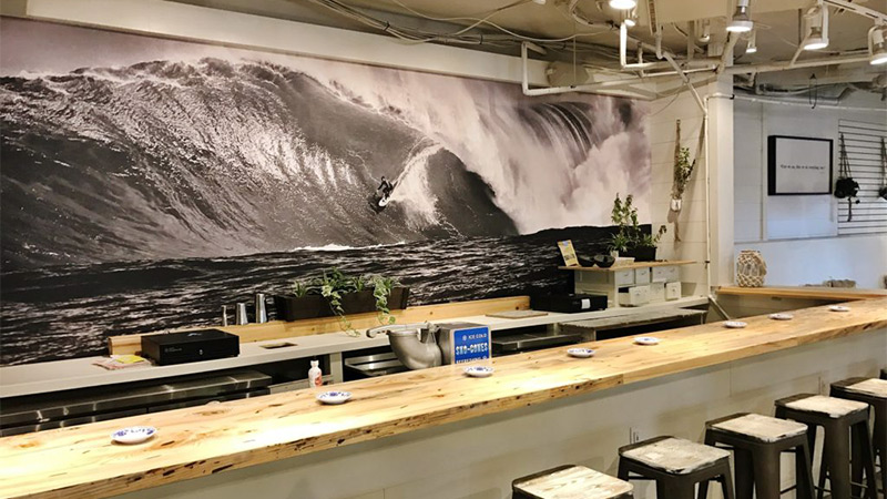 The Hideaway Restaurant in Bethany Beach, Delaware sports behind their front bar and food service counter a grayscale/black & white mural of a world-class surfer riding the waves off the coast of Hawaii.