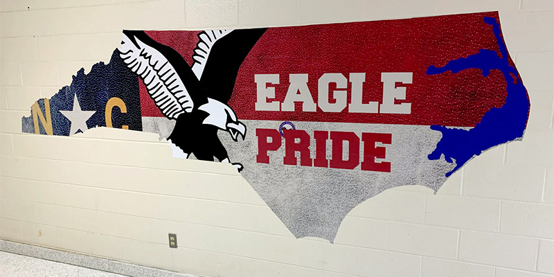 A large, die cut wall decal in the shape of the state of North Carolina features the Eagle Pride mascot and motto of Harnett Primary School. Contour cut stickers like this can really spruce up a cinder block wall.