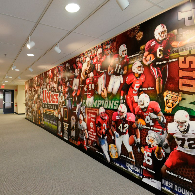 A large wallpaper mural featuring a collage of student athletes from the football team decorates the hall leading to the University of Massachusetts&rsquo; media room at the stadium. We can create similar wall graphics for schools and colleges of all sizes.