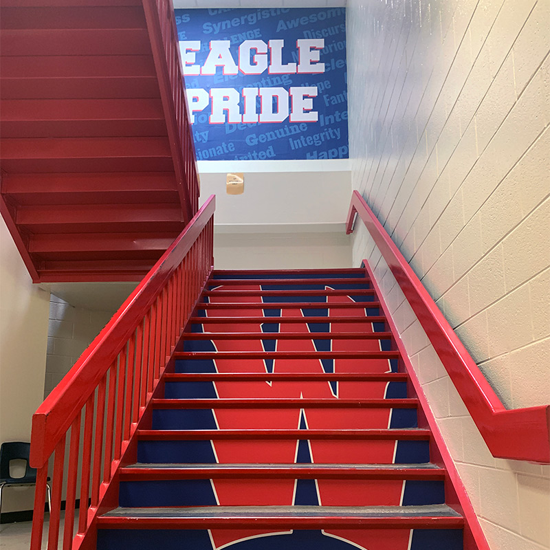 The stair risers at this school have been wrapped with decals that spell out the school’s “W” logo in this stairwell. The printed school mural greets students on the cinder block wall at the top of the stairway.