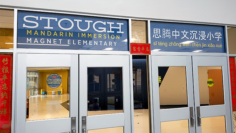 The glass window transoms above the entrance doors to Stough Magnet Elementary school have been covered with perforated window film printed with the schools name in school colors.