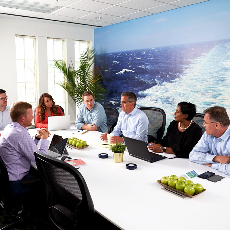 Executives meet in a sophisticated conference room decorated with a full sized printed wall mural of a large ships wake in the ocean.